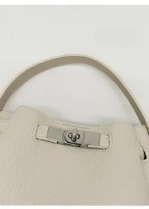 Détail macro du fermoir rotatif argenté sur le sac seau en cuir grainé crème