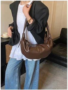 Detailed close-up of dark brown crescent bag showing soft leather folds and metal logo buckle