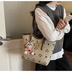 Detail of light brown tote bag with logo pattern, gold hardware and plush bear charm