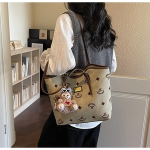Detail of olive canvas tote bag with leather trim and decorative bear charm accessory
