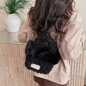Detail of black fuzzy plush handbag with silver bead chain and white woven label