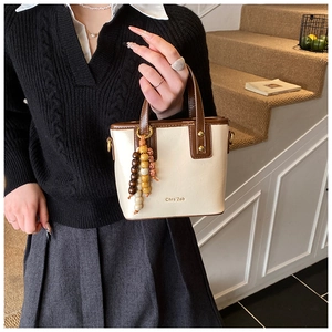 Detail of cream leather bucket bag with brown handles and vintage beaded charm