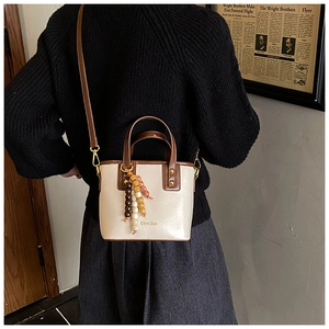 Detail of vintage beige bucket bag with brown leather strap and colorful bead charm