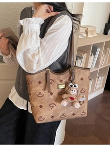 Vintage brown patterned tote bag with bear charm and slim handles in library setting