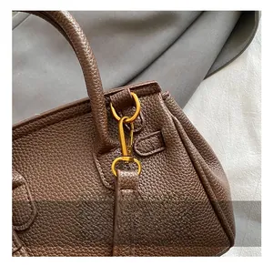 Close-up of golden metal D-ring hook and textured lychee pattern leather on brown handbag