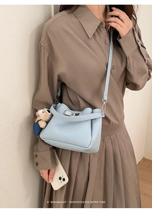 Détail du sac seau en cuir bleu clair à motif litchi avec charm ours et fermoir en métal