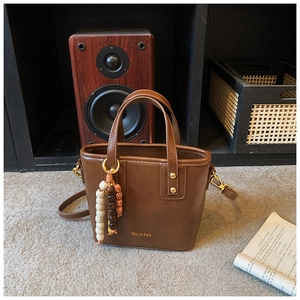 Detail of vintage brown bucket bag with beaded charm and gold logo on leather surface