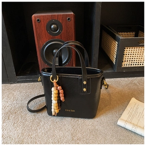 Detail of black vintage bucket bag featuring wooden bead pendant and gold hardware