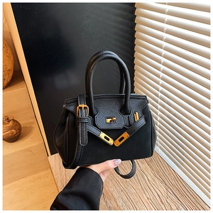 Detail of lychee pattern leather texture and golden metal swivel lock on black handbag