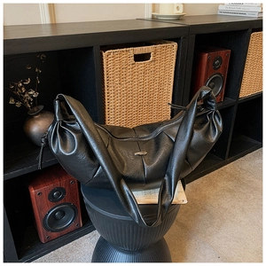Detail of black pleated croissant bag with soft texture and metal logo plaque