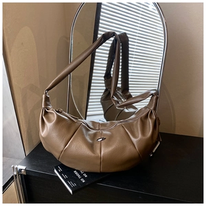 Detail of a brown pleated croissant bag with a silver metal buckle on a dark wood surface