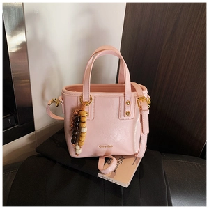 Pink leather bucket bag with wooden bead charm and gold hardware shown in detail