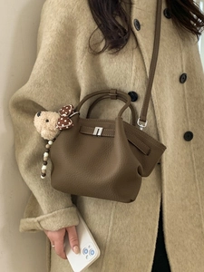 Brown lychee leather bucket bag with teddy bear charm shown on beige wool coat