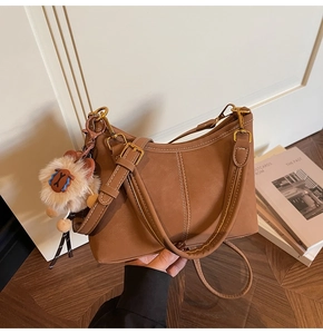 Detail of vintage brown suede bucket bag with bold stitching and a white plush charm