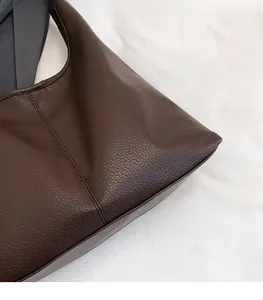 Detail of dark brown lychee leather texture and double stitching on a tote bag