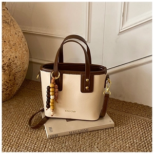 Close-up of a two-tone mini bucket bag with beaded charm and gold hardware on magazines