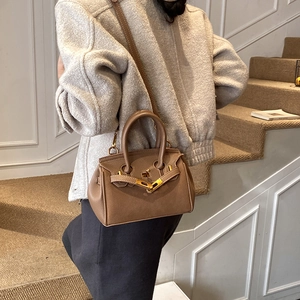 Detail of vintage brown litchi grain leather handbag with gold metal clasp on model