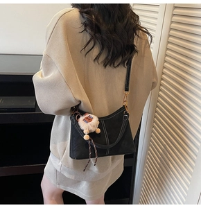 Detail of black crossbody bucket bag featuring white contrast stitching and a plush sheep charm