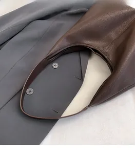 Close-up of dark brown lychee grain leather texture and handle on a large hobo bag