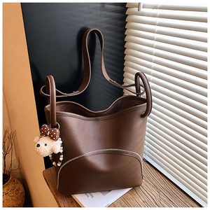 Detail of dark brown pebble leather tote bag featuring a cute bear charm and curved zipper