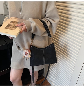 Detail of vintage black bucket bag with contrast stitching and plush charm on a model