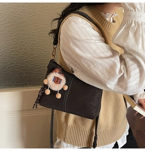 Detail of dark brown semi-moon bag with white contrast stitching and bear charm