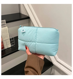 Macro detail of a light blue quilted pouch with triangle zipper pull and fabric texture