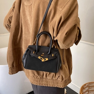 Minimalist black lychee leather handbag with gold metal lock worn by a model