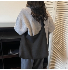 Back view of model wearing a large black minimalist hobo shoulder bag in matte fabric