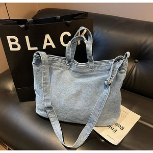 Detail of light blue denim tote bag with silver rivets and double handle on a black sofa