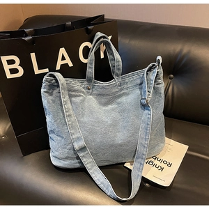 Close-up of light blue denim tote bag with metal buckle and stitching on black sofa