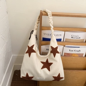 Detail view of cream-colored shoulder bag with brown plush star and ruched strap design