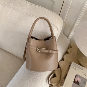 Détail du sac seau en cuir marron à motif litchi avec boucle argentée sur un canapé