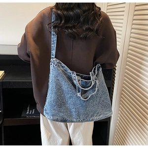 Detail of light blue denim tote bag worn as a shoulder bag on a casual outfit