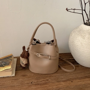 Détail du sac seau beige texture litchi avec pendentif ours sur table en bois