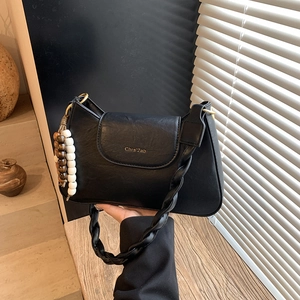 Détail du sac en similicuir noir avec bandoulière tressée et pendentif décoratif en perles