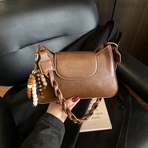 Détail d'un sac à bandoulière en cuir PU marron avec sangle tissée et breloque en bois