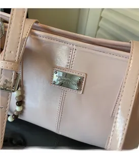 Detail of pink patent leather handbag with silver logo plate and beaded charm accessory