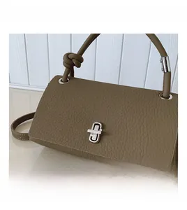 Detail view of khaki pebbled leather handbag with hardware lock and knotted strap