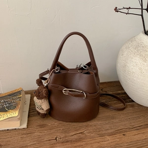 Gros plan détaillé d'un sac seau marron foncé avec pendentif ours sur table en bois