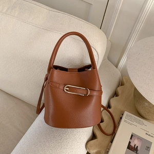 Détail du sac seau en cuir grainé caramel avec boucle en métal sur un canapé beige