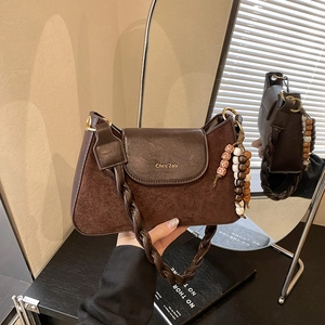 Détail d'un sac à bandoulière vintage en daim marron avec sangle tressée et breloque perlée