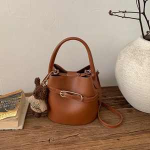 Détail d'un sac seau en cuir marron grainé avec un pendentif ours sur table en bois