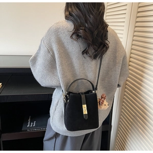 Détail d'un sac seau noir mat avec fermoir doré et breloque ours sur un pull gris