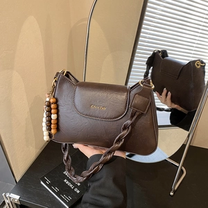Détail d'un sac à bandoulière marron foncé en similicuir avec bandoulière tressée et gland