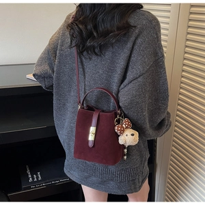 Détail du sac seau bordeaux en cuir mat avec serrure dorée et breloque ours