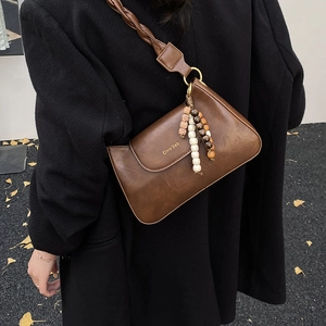 Détail du sac en cuir marron vintage avec bandoulière tressée et breloque bohème