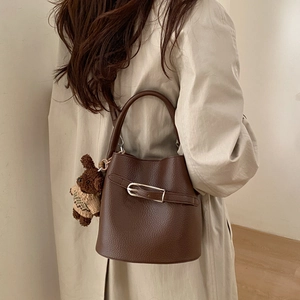 Détail du sac seau en cuir marron foncé avec boucle métallique et breloque ours