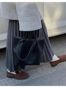 Outdoor street view of a black lychee texture leather bucket bag with top handle and strap