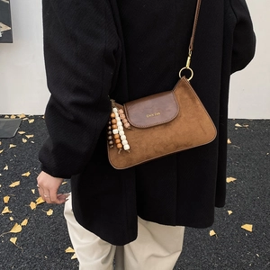 Détail d'un sac bandoulière vintage marron avec aspect cuir mat et breloque perlée